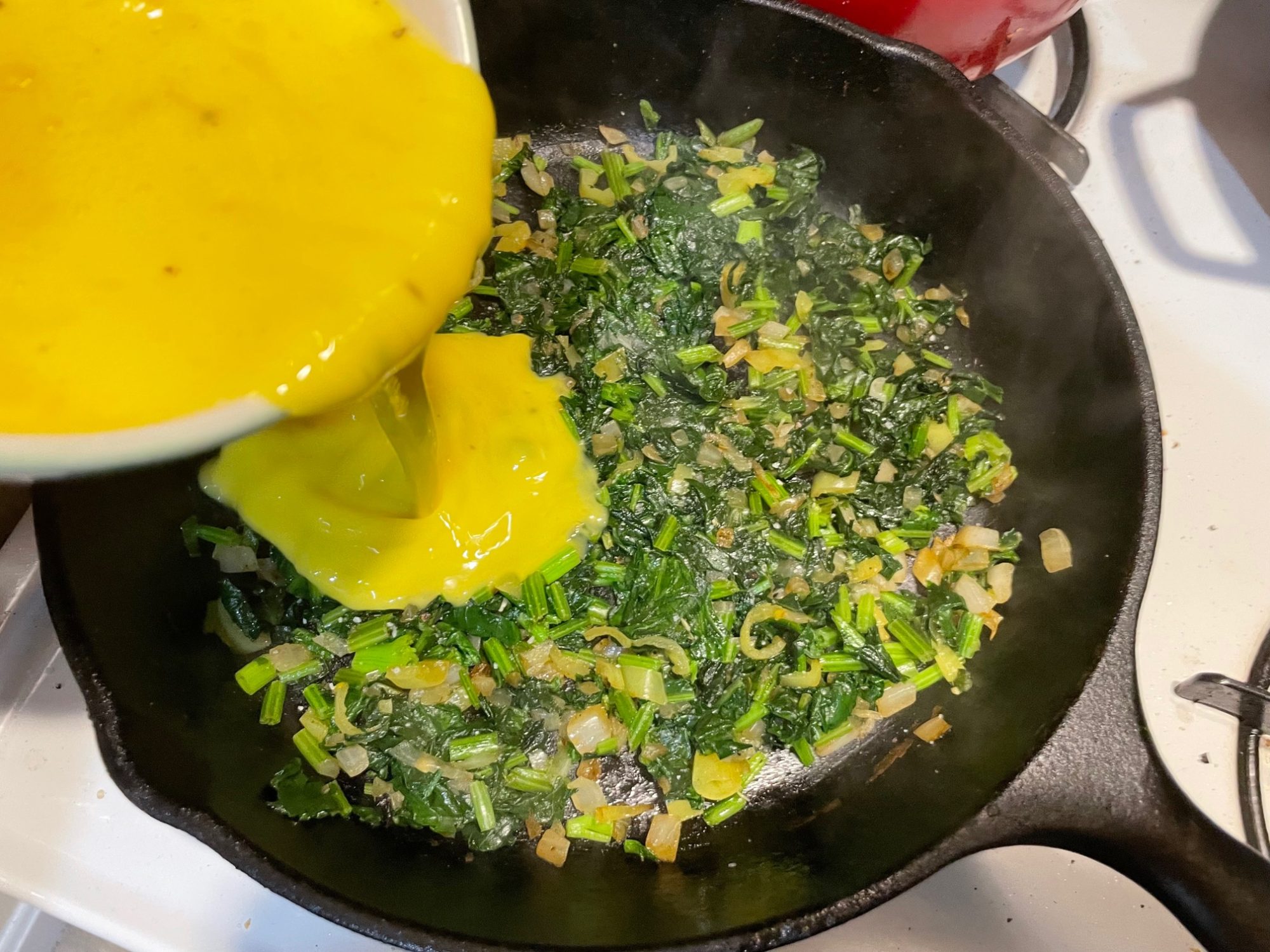 Adding eggs to the spinach mix in the pan before scrambling